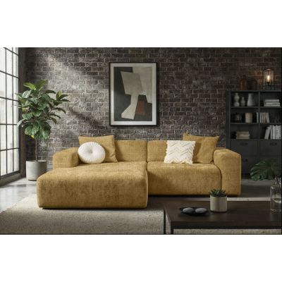 Ockerfarbene Eckcouch mit Longchair links im Bild und hellen Zierkissen vor einer dunklen Backsteinwand mit Regal und Zimmerpflanzen