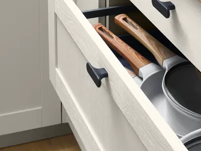 Detailansicht einer geöffneten Schublade mit weißen Rahmenfronten und schwarz matten Griffen im Landhausstil