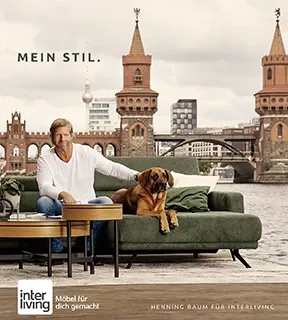 Schauspieler Henning Baum mit Hund auf Interliving Sofa am Flussufer vor Brücke – moderne Wohnstil-Inspiration bei Möbel Gruber mobil
