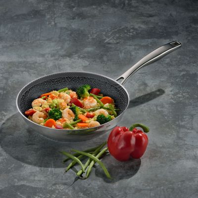 Edelstahlpfanne mit Gemüse auf einer dunklen Arbeitsfläche neben einer roten Paprika