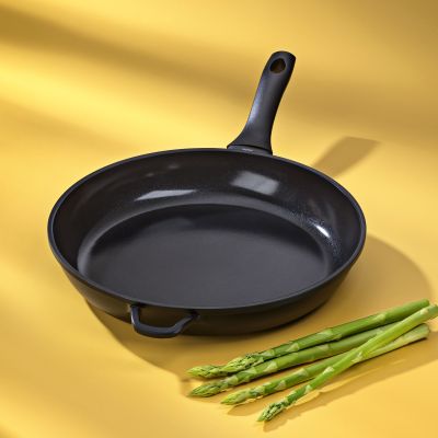 Leere schwarze Bratpfanne mit zwei Griffen neben grünem Spargel auf gelbem Untergrund