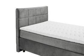 Boxspringbett „Voss 15 grey“ aus schräger Perspektive nahe am Kopfteil fotografiert, grauer Stoffbezug, Details der Matratze und des Toppers sichtbar