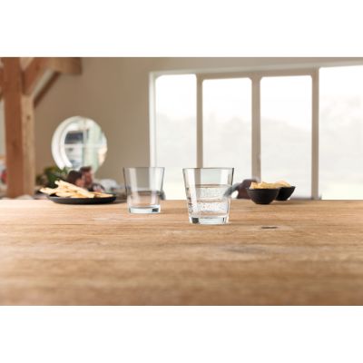 Zwei klare Trinkgläser auf Holztisch eines mit Wasser gefüllt im Hintergrund Snacks und Wohnraum