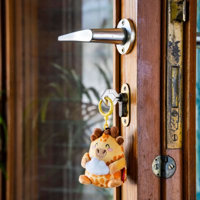 Giraffen-Plüsch-Schlüsselanhänger, an einer hölzernen Tür am Ring aufgehängt dargestellt.