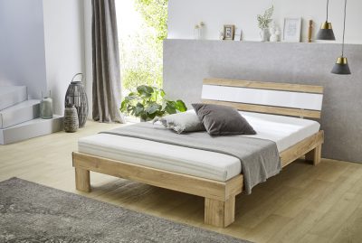 Minimalistisches Schlafzimmer mit Futonbett mit Matratze, grauer und weißer Bettwäsche, Pflanzen, modernem Dekor und natürlichem Licht.