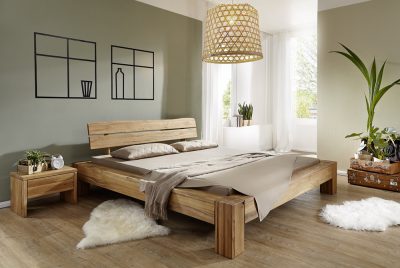 Minimalistisches Schlafzimmer mit massivem Bettgestell, grünen Wänden, geflochtener Hängelampe, weißem Teppich, Pflanzen und natürlichem Licht.