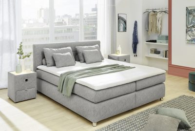Modernes Schlafzimmer von Möbel Gruber mit Boxspringbett, grüner Tagesdecke, Nachttischen und Blick auf die Stadt. Gemütliche, helle Einrichtung.