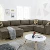 Wohnlandschaft von Möbel Gruber mit geblümten Kissen, rundem weißen Couchtisch, geometrischer Wandkunst und hoher Lampe.