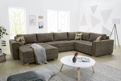 Wohnlandschaft von Möbel Gruber mit geblümten Kissen, rundem weißen Couchtisch, geometrischer Wandkunst und hoher Lampe.