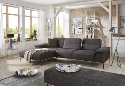 Modernes Wohnzimmer mit einem W.SCHILLIG Ecksofa, einer Akzentwand aus Ziegeln, großen Fenstern und einer Stehlampe.