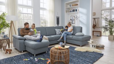 Familie entspannt auf einer Modulmaster Leder-Wohnlandschaft Toto L in einem hellen Wohnzimmer mit Büchern, Spielzeug und Pflanzen.