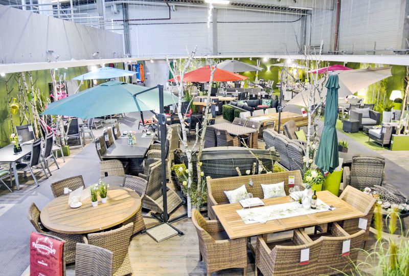Ein großer Showroom von Möbel Gruber präsentiert Outdoor-Möbelsets mit bunten Sonnenschirmen und Pflanzen in einem hellen, offenen Raum.