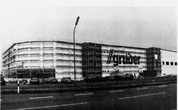 Schwarzweißfoto eines großen Gebäudes im Bau, mit Gerüst und deutlich sichtbarem „Möbel Gruber“-Schild.