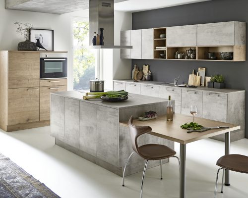Moderne Küche mit Schränken aus Beton und Holz, Kochinsel mit Herd, Esstisch mit zwei Stühlen, großem Fenster und Dekor.