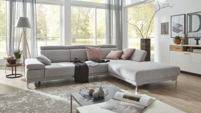 Modernes Wohnzimmer mit einem grauen Sofa, Kissen, einer Lampe und großen Fenstern mit transparenten Vorhängen. Brauner Teppich auf dem Boden.