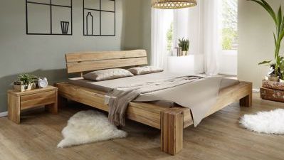 Ein gemütliches Schlafzimmer mit einem Holzbett, beiger Bettwäsche, einem Nachttisch und einem flauschigen Teppich. Natürliches Licht fällt durch transparente Vorhänge.