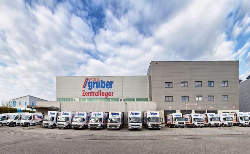 Außenansicht des Lagers von Möbel Gruber mit mehreren davor geparkten Lieferwagen unter einem bewölkten Himmel.