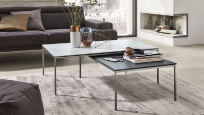 Modernes Wohnzimmer mit grauem Sofa, verschachtelten Couchtischen, Dekoartikeln und einem Kamin im Hintergrund.