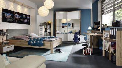 Modernes Schlafzimmer mit Holzbett, blauen Akzenten, Schreibtisch mit Computer, Regal und Kleiderschrank. Von der Decke hängen Pendelleuchten.