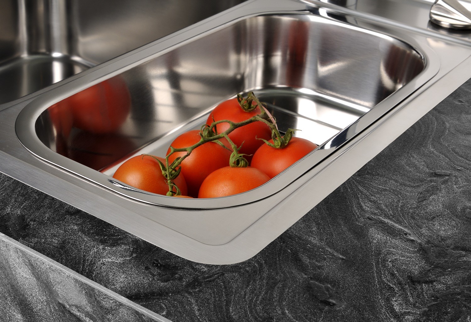 Fünf Tomaten an einer Rebe in einer Küchenspüle aus Edelstahl mit einer Arbeitsplatte aus dunklem Marmor.