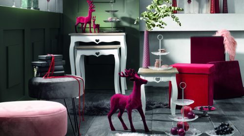 Stilvolles Wohnzimmer von Möbel Gruber: rosa Hirschfiguren, plüschige Hocker, flauschige Teppiche und edle Glaswaren vor grünen Wänden.