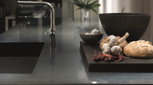 Moderne Küche mit elegantem Wasserhahn, dunkler Arbeitsplatte und einem Schneidebrett mit Brot, Knoblauch und getrockneten Paprika.