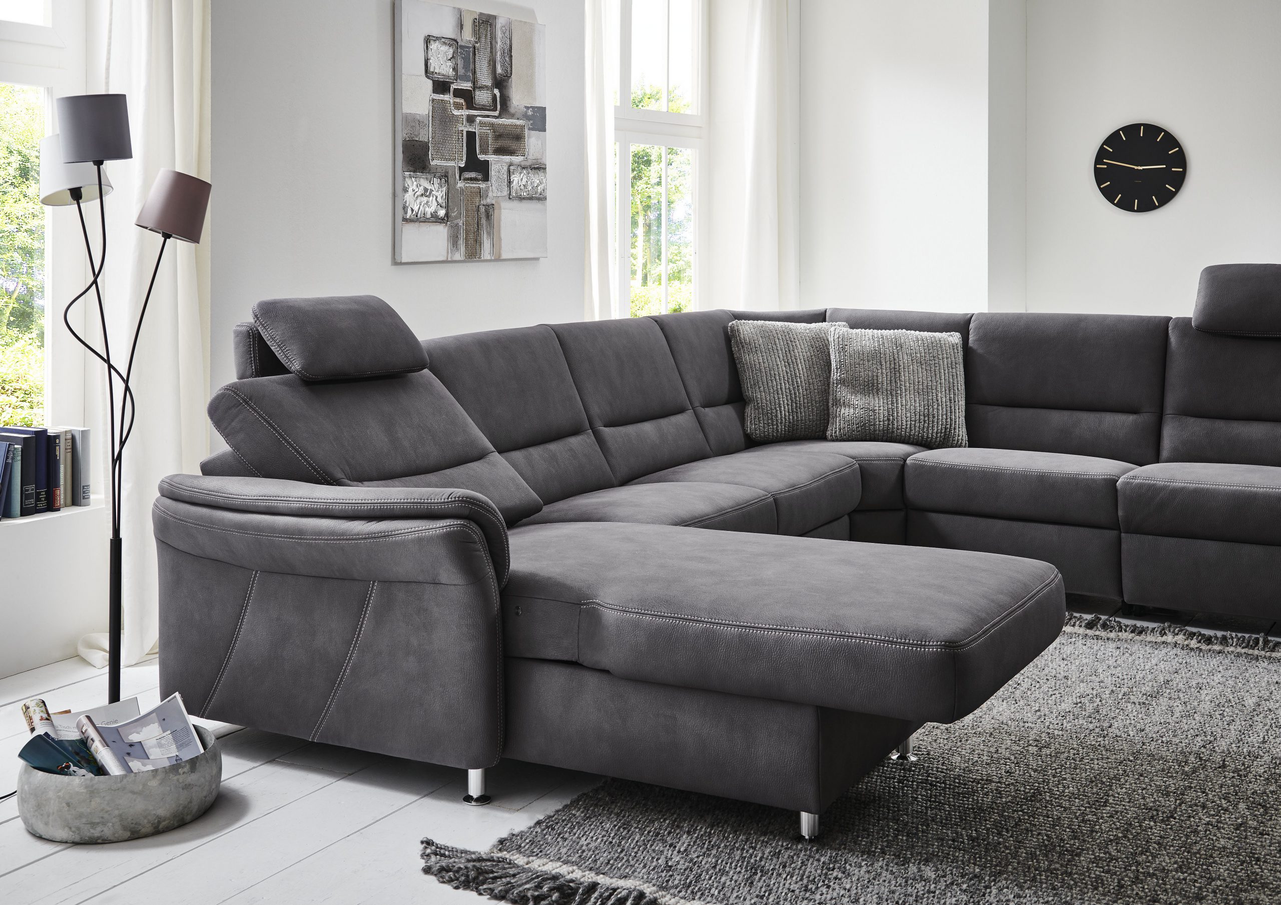 Modernes Wohnzimmer mit grauem Sofagarnitur von Möbel Gruber, strukturierten Kissen, einer Stehlampe und großen Fenstern.