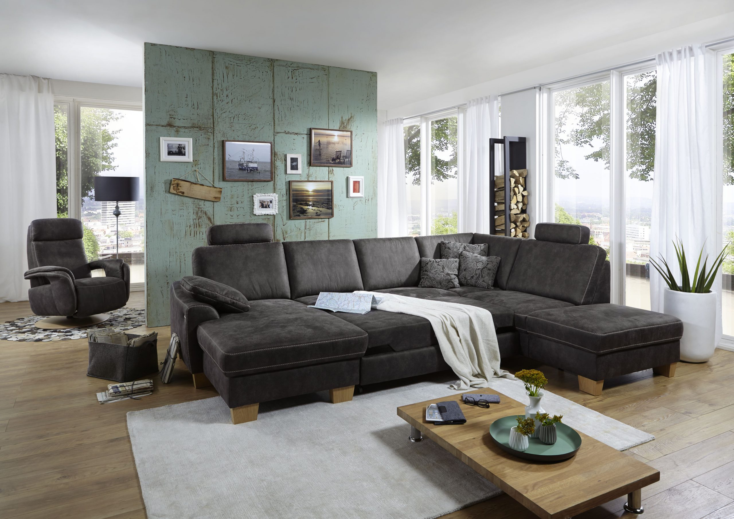 Modernes Wohnzimmer mit großem Sofagarnitur von Möbel Gruber, Couchtisch aus Holz, dekorativer Wand und Fenstern mit Panoramablick.