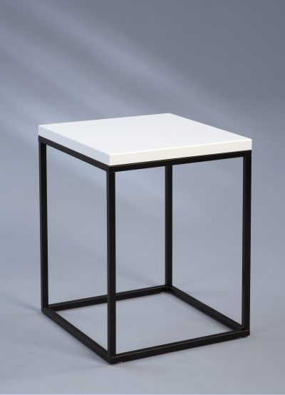Der Beistelltisch von Möbel Gruber ist ein quadratischer Hocker mit weißer Sitzfläche und schwarzem Metallrahmen auf grauem Hintergrund.