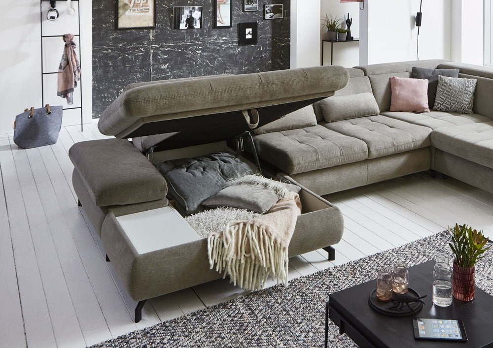 Modernes Wohnzimmer von Möbel Gruber mit einem grauen Sofagarnitur mit Stauraum, Kissen und einer Tafelwand.