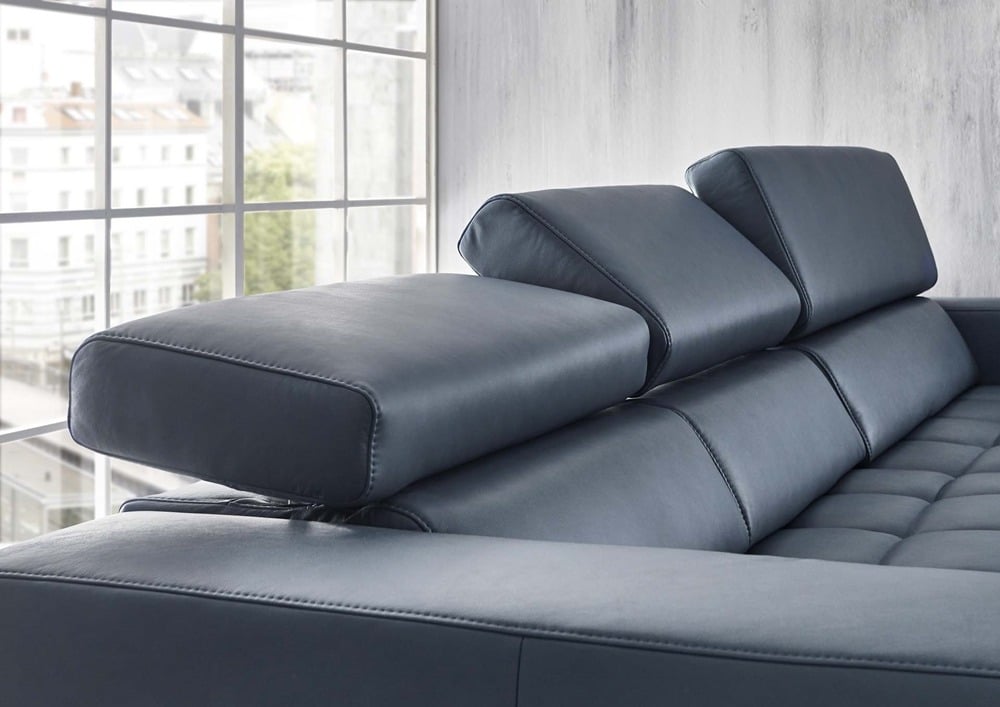 Nahaufnahme eines modernen grauen Sofas von Möbel Gruber mit verstellbaren Kopfstützen in einem hellen Raum neben einem großen Fenster.