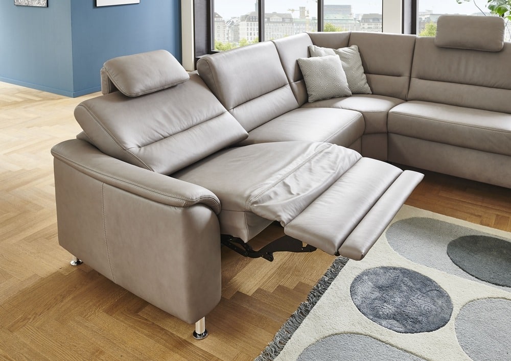 Ein modernes hellgraues Sofa mit Liegestuhl, Kissen und geometrischem Teppich von Möbel Gruber erhellt den Raum mit Holzboden.