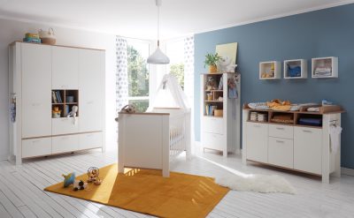 Das moderne Babyzimmer von Möbel Gruber verfügt über weiße Möbel, eine blaue Akzentwand, ein Kinderbett, einen Wickeltisch und einen gelben Teppich auf Holzboden.