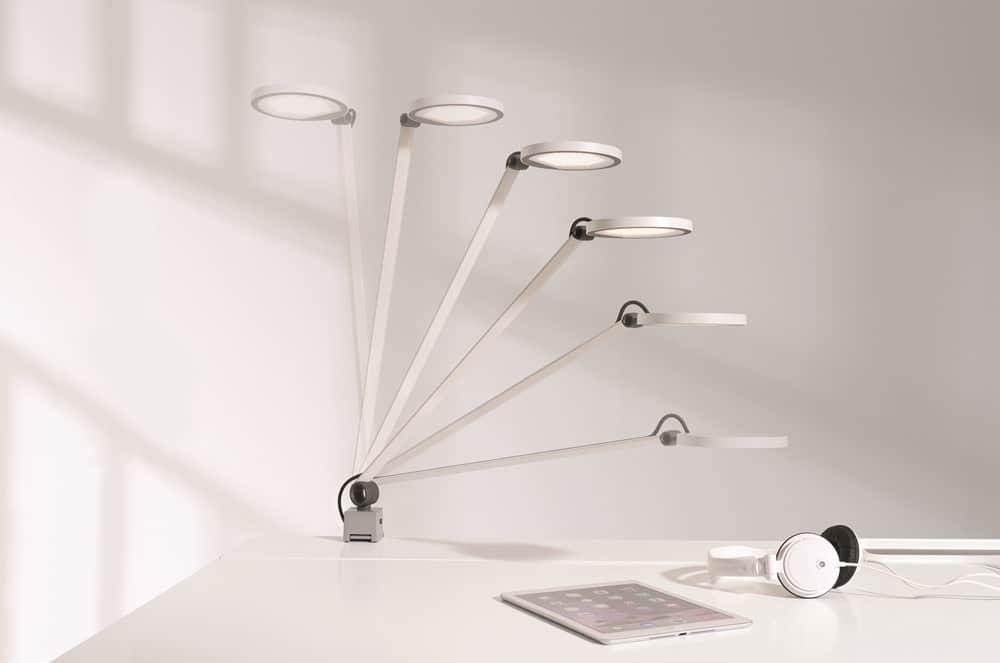 Verstellbare Schreibtischlampe mit rundem Licht von Möbel Gruber, präsentiert neben Kopfhörern und einem Tablet auf einer weißen Oberfläche.