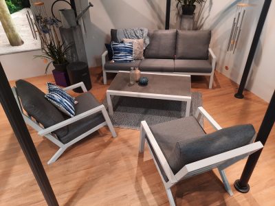 Terrassenset „Loungegruppe“ von Möbel Gruber mit grauem Sofa, Stühlen, Tisch und blaugrauen Kissen auf einer Holzterrasse.