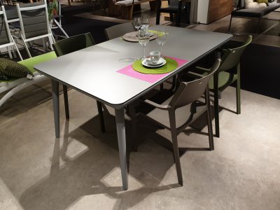 Ein moderner Gartengruppen-Esstisch mit sechs Stühlen, gedeckt mit Tellern, Tassen und Gläsern auf bunten Tischsets.