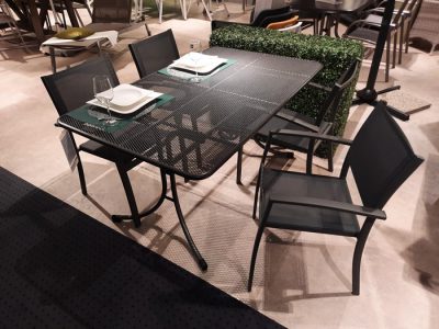 Ein modernes Garten-Essset von Möbel Gruber mit vier Metallstühlen und einem rechteckigen Glastisch, garniert mit Tellern und Gläsern.