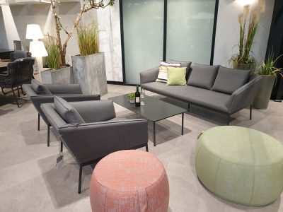 Modernes Wohnzimmer von Möbel Gruber mit Lounge-Set 4-tlg. mit grauem Sofa, Sesseln und bunten Ottomanen.