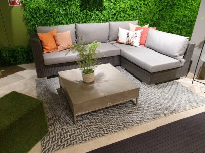 Ein moderner Wohnbereich mit dem grauen Gartengruppe-Sofa, einem quadratischen Couchtisch und einer grünen Wandkulisse.