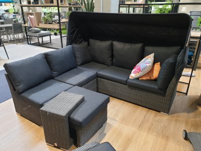 Muschelset 5-tlg. Rattansofa mit dunklen Polstern und bunten Kissen auf einem hölzernen Ausstellungsraumboden.