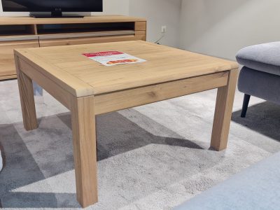 Ein Interliving Couchtisch mit einer Möbel Gruber Broschüre steht auf einem hellen Teppich im Wohnzimmer.