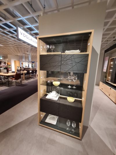 Eine Voglauer Vitrine von Möbel Gruber, die Geschirr und Gläser im modernen Glasvitrinenstil präsentiert.