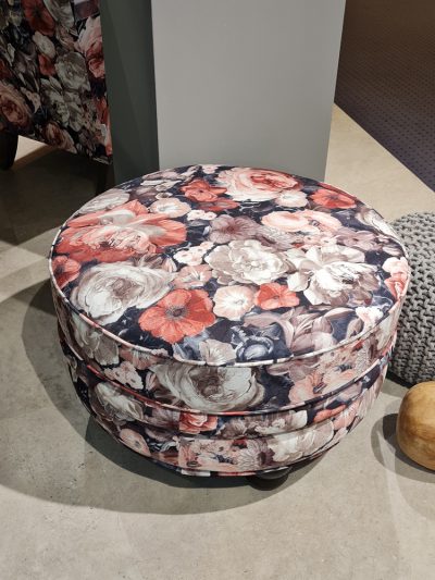Ein runder Hocker von Möbel Gruber hat ein rosa, rotes und graues Blumenmuster auf einem Betonboden.