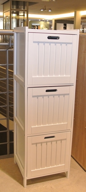 Bad-/Wohnregal von Möbel Gruber: ein hoher weißer Schrank mit drei Schubladen, jede mit einem rechteckigen Griff, in einem Ausstellungsraum.