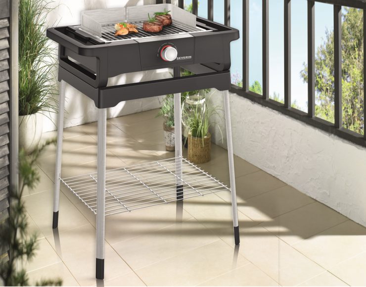 Auf einem Balkon von Möbel Gruber brutzelt ein Elektrogrill Steaks inmitten üppiger Topfpflanzen und eines eleganten Geländers.