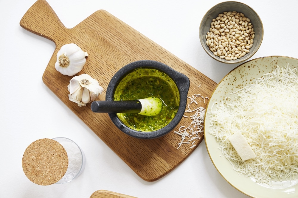 Ein Mörser mit Pesto, Knoblauch, Pinienkernen und Parmesan auf einem Holzbrett von Möbel Gruber sorgt für eine rustikale italienische Atmosphäre.