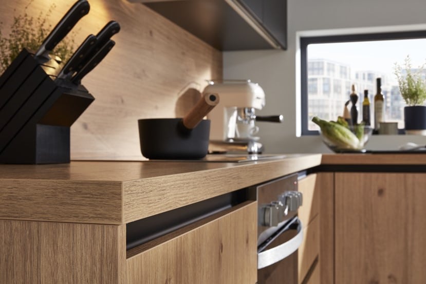 Moderne Küche von Möbel Gruber mit Holzschränken, Messerset, schwarzem Topf und weißem Mixer. Sonnenlicht fällt wunderschön hinein.