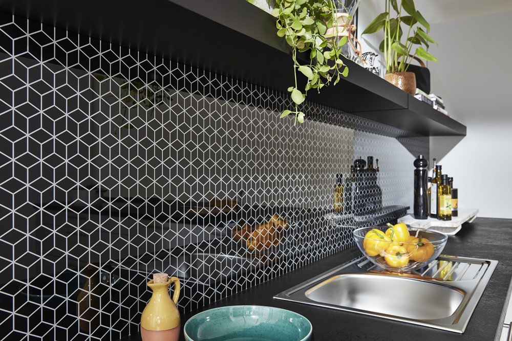 Moderne Küche von Möbel Gruber mit schwarzer geometrischer Fliesenrückwand, Edelstahlspüle und Regalen mit Pflanzen.