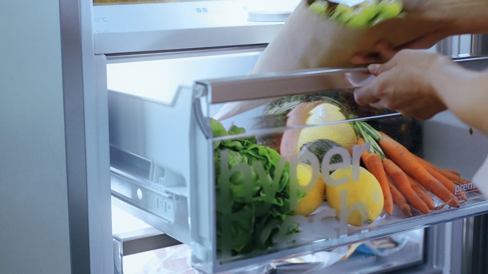 Person legt frische Produkte wie Salat, Zitronen und Karotten in eine Kühlschrankschublade von Möbel Gruber.
