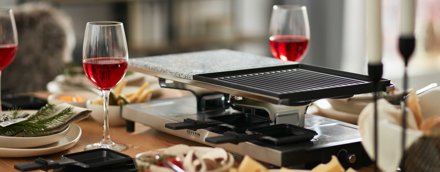 Ein Esstisch von Möbel Gruber mit Raclette-Grill, Rotweingläsern und Weihnachtsdekoration.